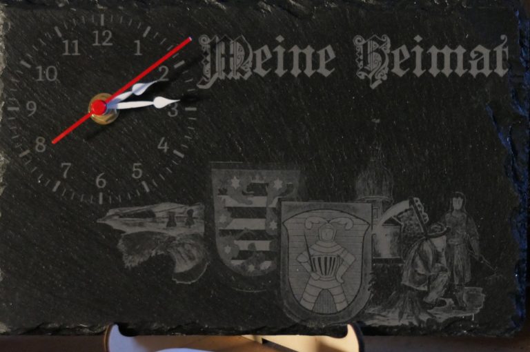 Meine Heimat Wanduhr mit dem Schriftzug „Meine Heimat“ und mehreren Wappen und Motiven.